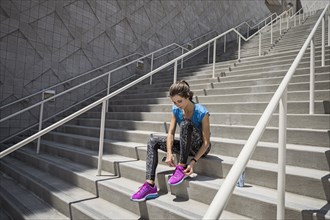 Caucasian woman sitting on staircase tying shoelace