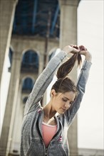 Caucasian woman stretching under overpass holding ponytail