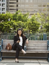 Chinese businesswoman texting on cell phone on city bench