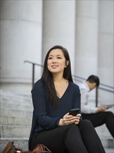 Chinese businesswoman sitting on staircase holding cell phone