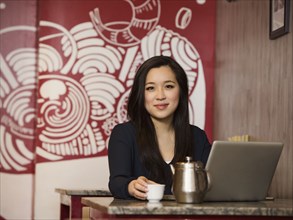 Chinese businesswoman drinking tea and using laptop