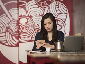 Chinese businesswoman texting on cell phone in restaurant