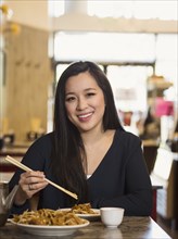 Chinese woman eating with chopsticks in restaurant