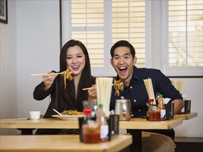 Smiling Chinese couple holding noodles with chopsticks in restaurant