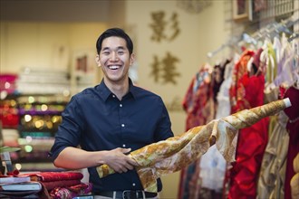 Smiling Chinese man posing with fabric in store