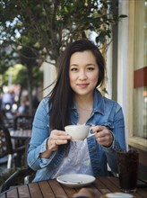 Smiling Chinese woman drinking coffee at outdoor cafe
