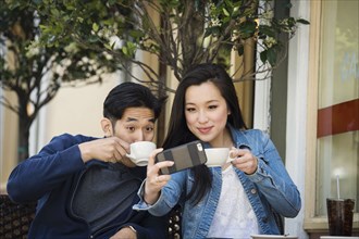 Smiling Chinese couple posing for cell phone selfie at outdoor cafe