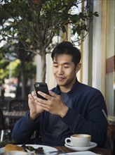 Smiling Chinese man texting on cell phone at outdoor cafe