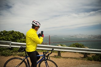 Hispanic man on bicycle photographing waterfront with cell phone