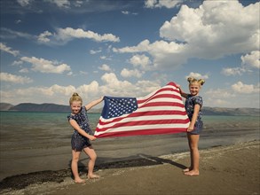 Caucasian girls holding American flag at beach