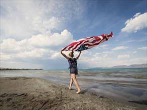 Caucasian girl walking with American flag at beach