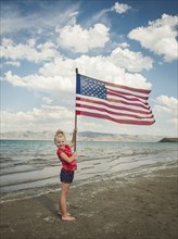 Caucasian girl holding American flag at beach