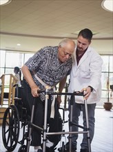 Physical therapist helping man in wheelchair use walker
