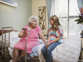 Smiling Caucasian woman sitting on bed talking to granddaughter