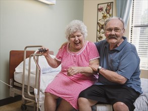 Caucasian man sitting on bed hugging laughing woman