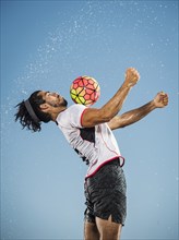 Water spraying on Hispanic man trapping soccer ball on chest