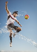 Water spraying on Hispanic man heading soccer ball