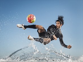Water spraying on Hispanic man kicking soccer ball