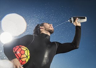 Hispanic man holding soccer ball spraying water into mouth