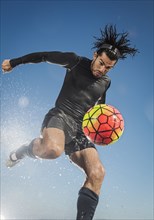 Water splashing on Hispanic man kicking soccer ball