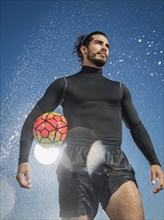 Water splashing on Hispanic man holding soccer ball