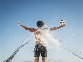 Water splashing on back of Hispanic man holding soccer ball