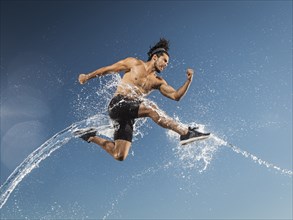 Water splashing on Hispanic man running and jumping