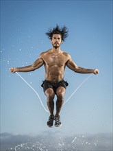 Water splashing on Hispanic man jumping rope