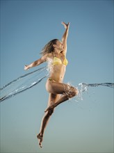 Water splashing on Caucasian woman jumping in bikini