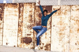 African American woman jumping for joy near rusty metal wall