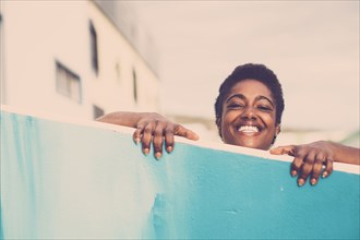 Smiling African American woman peering over blue wall