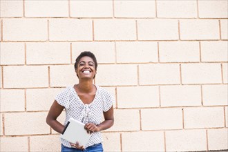 Smiling African American woman holding digital tablet near concrete wall