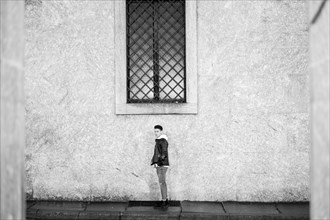Portrait of distant man standing underneath window on sidewalk