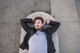 Caucasian man laying on concrete smoking cigarette