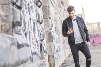 Smiling Caucasian man walking on sidewalk texting on cell phone