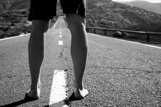 Legs of barefoot Caucasian man standing in middle of road