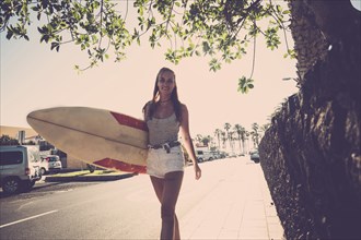 Caucasian woman walking on sidewalk carrying surfboard