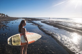 Caucasian woman standing on beach holding surfboard