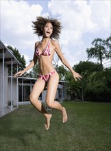 Mixed race woman in bikini jumping in backyard