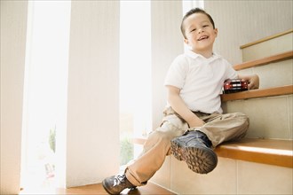 Hispanic boy sitting on staircase with toy car