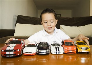 Hispanic boy lining up toy cars