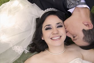 Hispanic bride and groom laying on ground