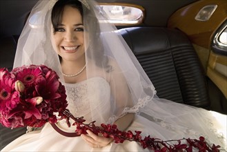 Hispanic bride sitting with bouquet in car