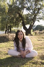 Laughing Hispanic woman sitting in grass