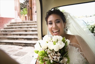 Hispanic bride sitting with bouquet in back of car