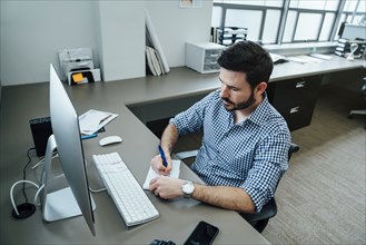 Caucasian businessman writing notes at a computer