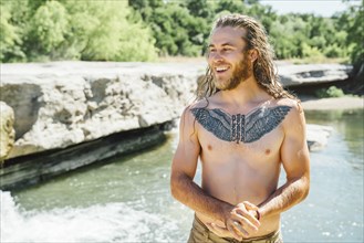 Smiling Caucasian man with chest tattoo standing near river