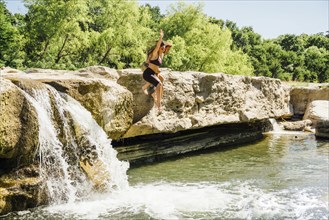 Caucasian couple jumping off rocks near waterfalls