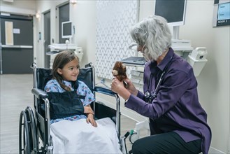 Doctor showing teddy bear to girl in wheelchair