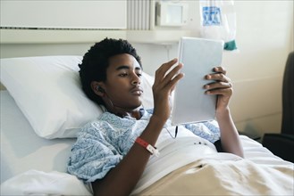 Black boy in hospital bed listening to digital tablet